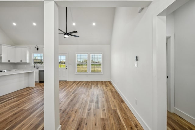 unfurnished living room with high vaulted ceiling, a sink, light wood finished floors, baseboards, and ceiling fan