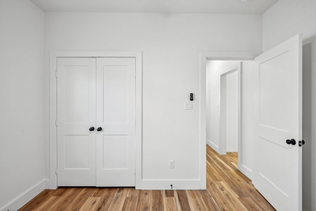 unfurnished bedroom with light wood-style flooring, baseboards, and a closet