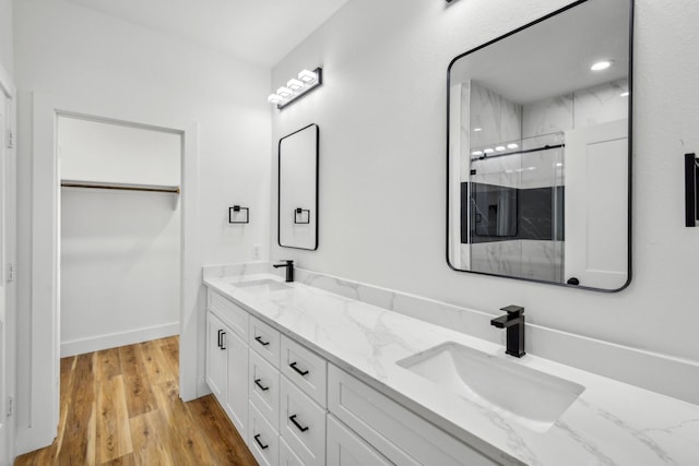 bathroom featuring a walk in closet, wood finished floors, a marble finish shower, and a sink
