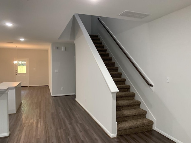 stairs featuring visible vents, wood finished floors, baseboards, and a chandelier