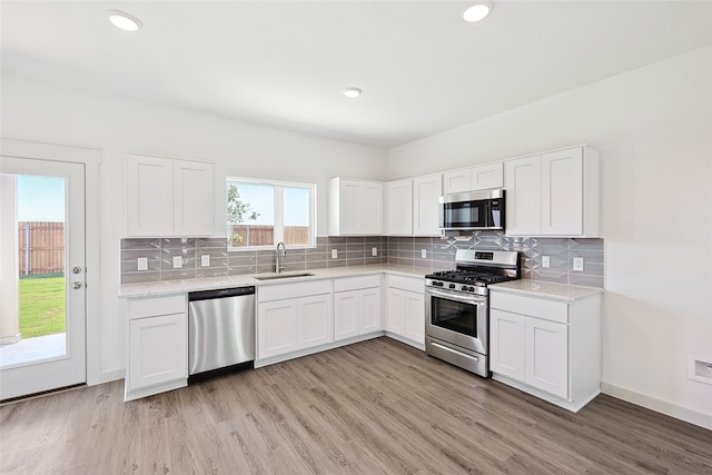 4314 Maple Root Ln, Pinehurst, TX 77362 - kitchen featuring appliances with stainless steel finishes, a sink, light wood finished floors, white cabinets, and backsplash
