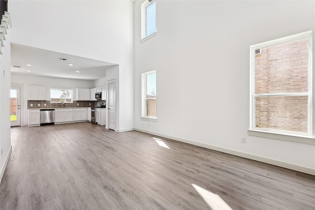 4314 Maple Root Ln, Pinehurst, TX 77362 - unfurnished living room featuring light wood-style floors, a high ceiling, baseboards, a sink, and recessed lighting