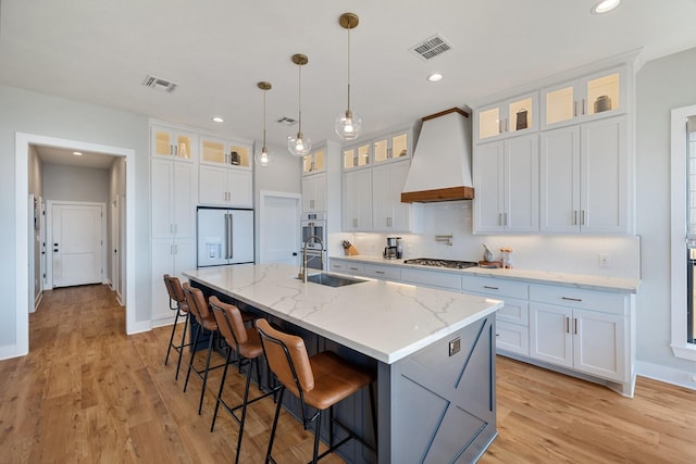 kitchen with high end fridge, a sink, stainless steel gas cooktop, premium range hood, and visible vents