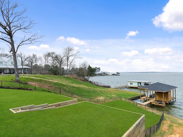 view of dock with fence, a lawn, boat lift, and a water view