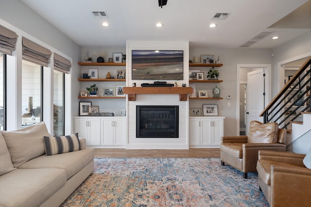 living area featuring light wood-style flooring, visible vents, a fireplace, and stairway