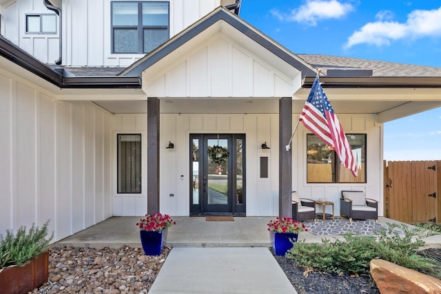 doorway to property featuring roof with shingles, a porch, board and batten siding, and fence