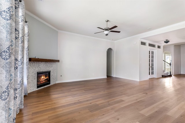 23509 Red Juniper Ln, New Caney, TX 77357 - unfurnished living room featuring arched walkways, wood finished floors, a ceiling fan, a tiled fireplace, and ornamental molding