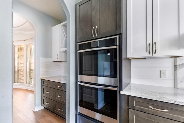23509 Red Juniper Ln, New Caney, TX 77357 - kitchen featuring double oven, arched walkways, light stone counters, wood finished floors, and dark brown cabinets