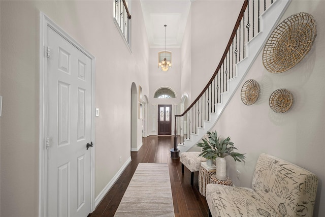 foyer entrance with baseboards, stairway, dark wood-style floors, arched walkways, and a notable chandelier
