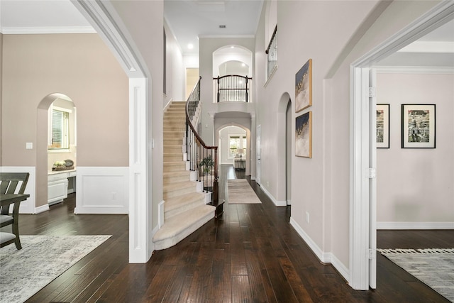 entrance foyer with a healthy amount of sunlight, crown molding, dark wood finished floors, stairs, and arched walkways