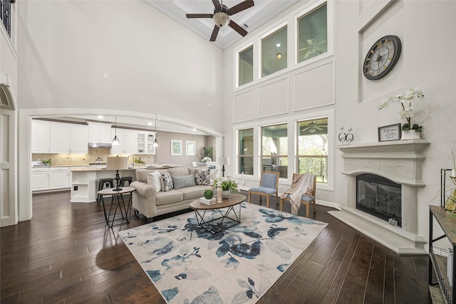 living area featuring a glass covered fireplace, dark wood-style floors, a ceiling fan, and high vaulted ceiling