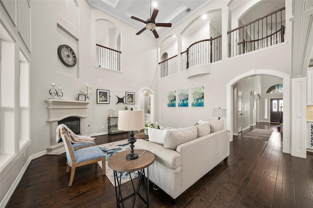 living area featuring a ceiling fan, baseboards, arched walkways, dark wood-type flooring, and a glass covered fireplace