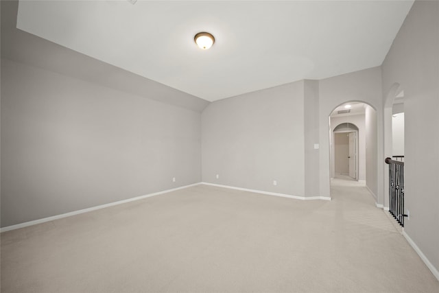 empty room with baseboards, arched walkways, light colored carpet, and vaulted ceiling