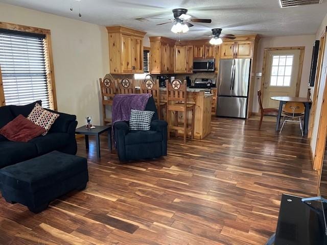 living room featuring visible vents, dark wood-type flooring, and ceiling fan