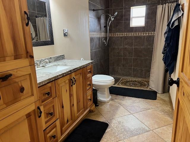 full bathroom featuring toilet, tiled shower, and vanity