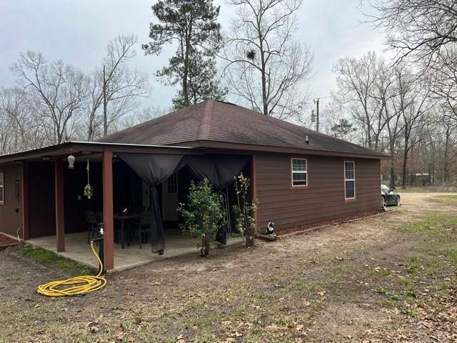 view of side of home featuring a shingled roof and a patio area