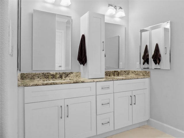 full bath featuring baseboards, double vanity, and a sink