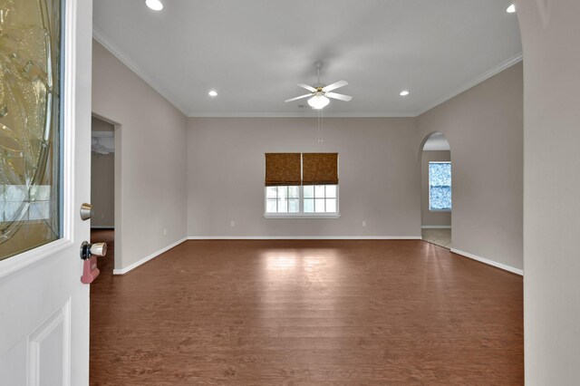 empty room with baseboards, arched walkways, dark wood-style flooring, ornamental molding, and ceiling fan