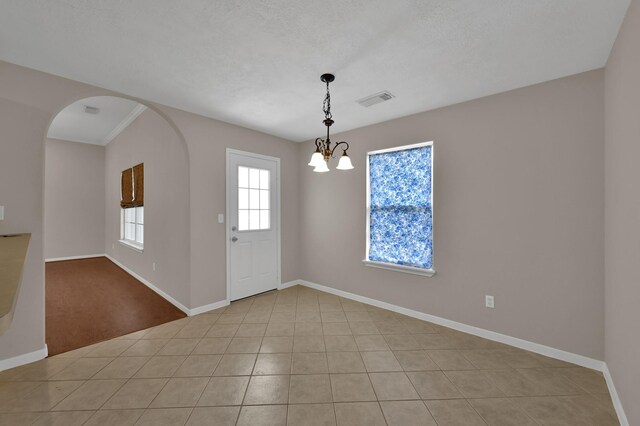empty room with visible vents, a notable chandelier, arched walkways, light tile patterned flooring, and baseboards