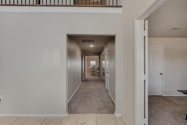 hall featuring visible vents, light colored carpet, and light tile patterned flooring