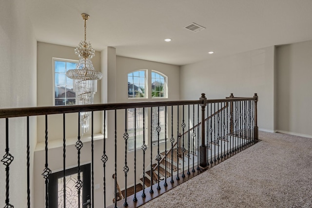 hallway featuring an inviting chandelier, carpet flooring, visible vents, and plenty of natural light