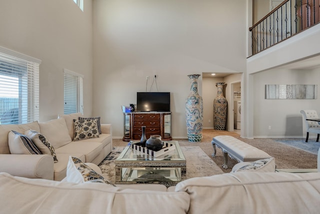carpeted living area with plenty of natural light, washer / dryer, baseboards, and a towering ceiling