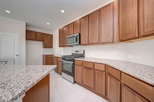 kitchen featuring brown cabinetry, light stone countertops, recessed lighting, appliances with stainless steel finishes, and light tile patterned floors