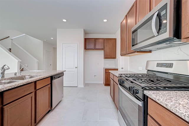 kitchen featuring brown cabinetry, a sink, light stone counters, stainless steel appliances, and recessed lighting