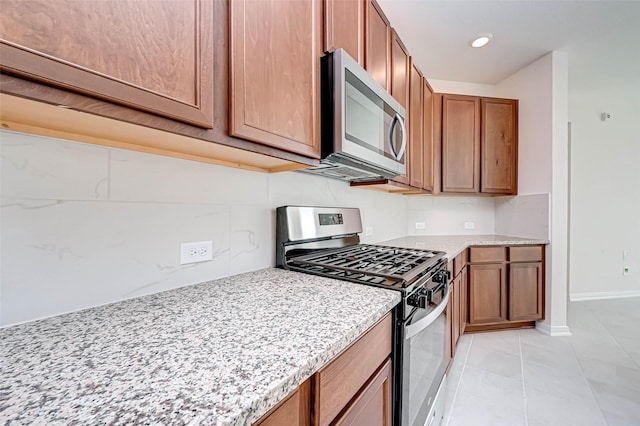 kitchen with brown cabinets, light tile patterned flooring, appliances with stainless steel finishes, and light stone counters