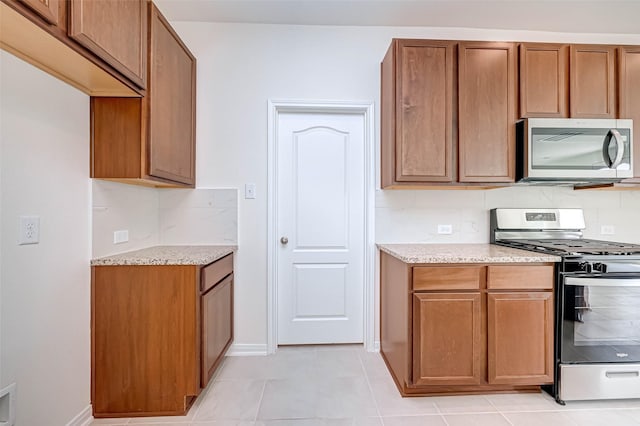 kitchen featuring brown cabinets, light stone countertops, appliances with stainless steel finishes, and decorative backsplash