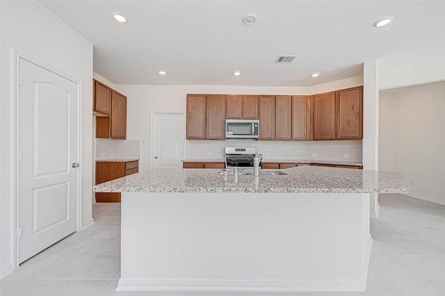 kitchen with brown cabinets, stainless steel appliances, visible vents, and light tile patterned floors