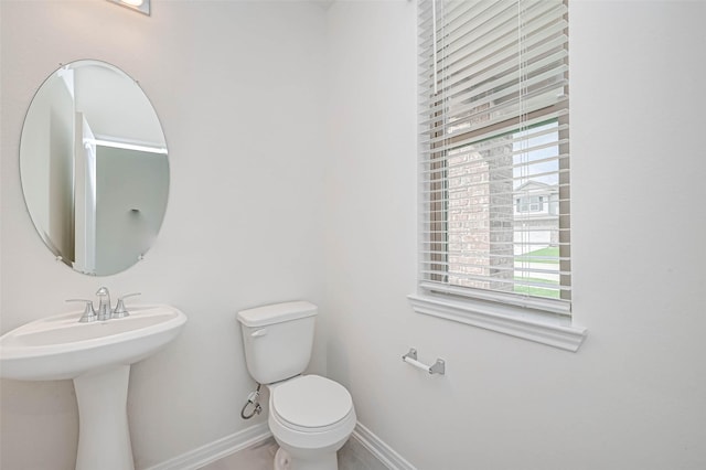 half bath featuring baseboards and toilet