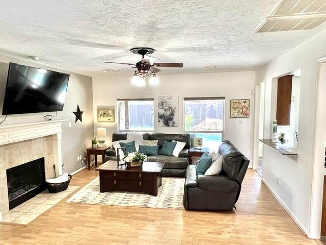living area with visible vents, wood finished floors, a fireplace, a textured ceiling, and a ceiling fan