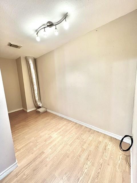 spare room with a textured ceiling, baseboards, visible vents, and light wood-style flooring