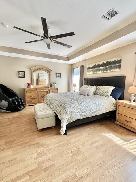 bedroom featuring a ceiling fan, light wood-type flooring, a tray ceiling, visible vents, and ornamental molding