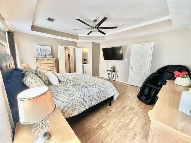 bedroom with visible vents, ornamental molding, wood finished floors, and a raised ceiling