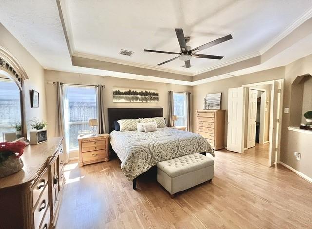 bedroom with visible vents, light wood-style flooring, and a raised ceiling