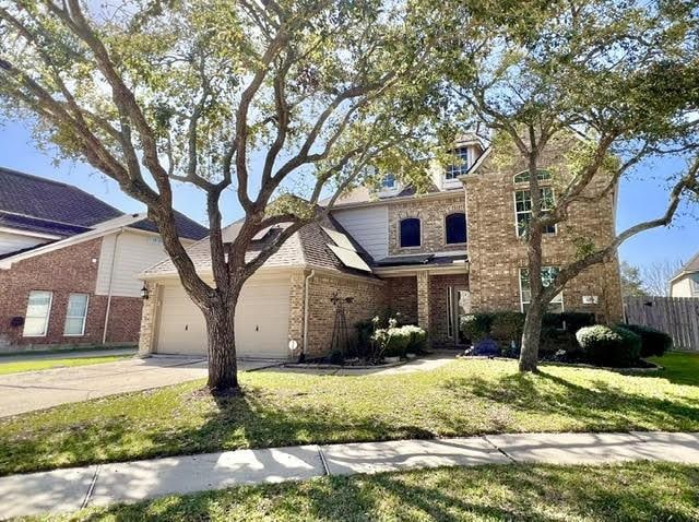traditional-style house with fence, an attached garage, a front lawn, brick siding, and concrete driveway