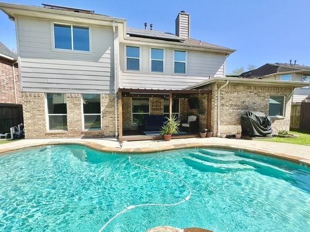 back of property featuring a patio area, solar panels, an outdoor pool, and brick siding
