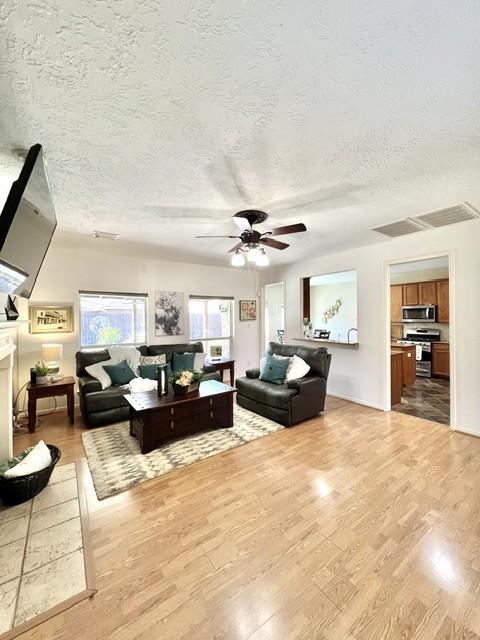 living room with light wood-style floors, ceiling fan, a textured ceiling, and visible vents