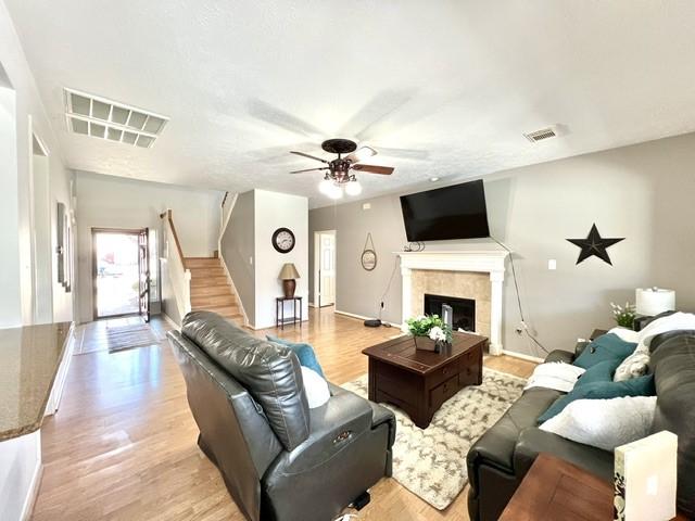 living area with ceiling fan, light wood-type flooring, stairs, and visible vents