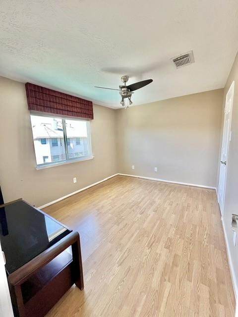 empty room featuring visible vents, a ceiling fan, light wood finished floors, and baseboards