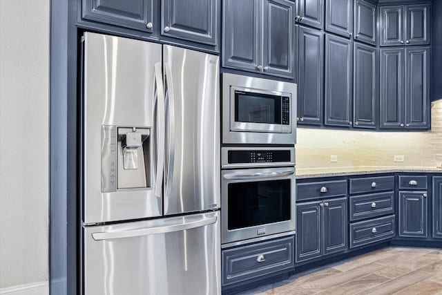 kitchen featuring blue cabinetry, backsplash, light stone counters, light wood-style flooring, and appliances with stainless steel finishes