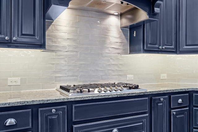 kitchen with blue cabinets, wall chimney range hood, backsplash, and stainless steel gas cooktop
