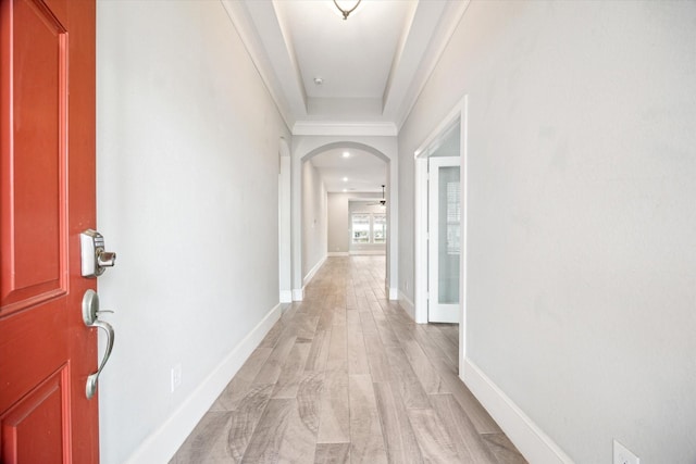hall with baseboards, arched walkways, and light wood-style flooring