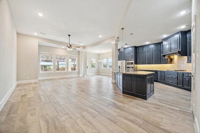 kitchen featuring a center island with sink, under cabinet range hood, backsplash, open floor plan, and appliances with stainless steel finishes