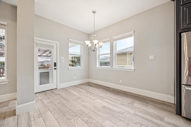 unfurnished dining area with an inviting chandelier, light wood-style floors, and baseboards