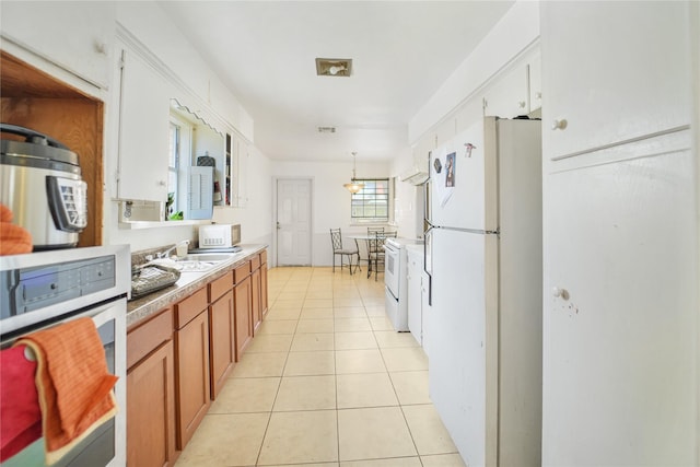 kitchen featuring brown cabinetry, light countertops, light tile patterned flooring, white appliances, and a sink