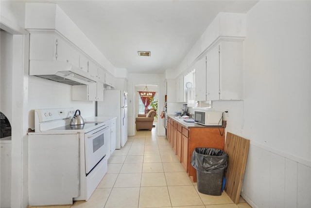 kitchen featuring visible vents, under cabinet range hood, light tile patterned floors, wainscoting, and white appliances