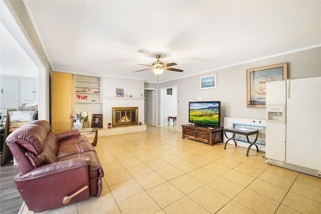 living room with a ceiling fan, built in features, crown molding, light tile patterned floors, and a brick fireplace